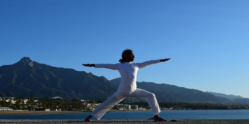 Silhouette of a person in a powerful yoga warrior pose against a sunrise.